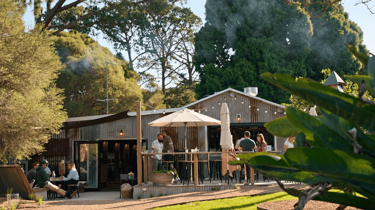 Outside view of the whiskery with people standing and sitting and enjoying a sunny afternoon, there is smoke across the top of the image indicating a wood fire is burning nearby.